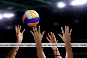 hand blocking volleyball spike over the net inside of a stadium